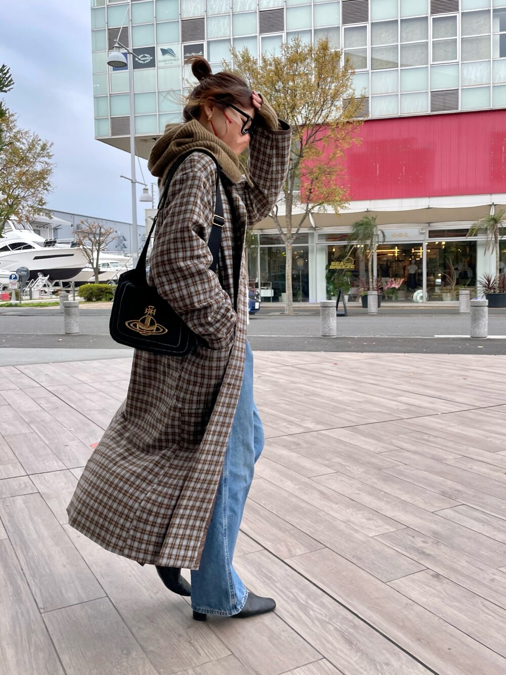 グレー系のステンカラーコート、ブルー系のデニムパンツ、ブラウン系のネックウォーマー/スヌードを着用したレディースの冬コーディネートの3枚目の写真