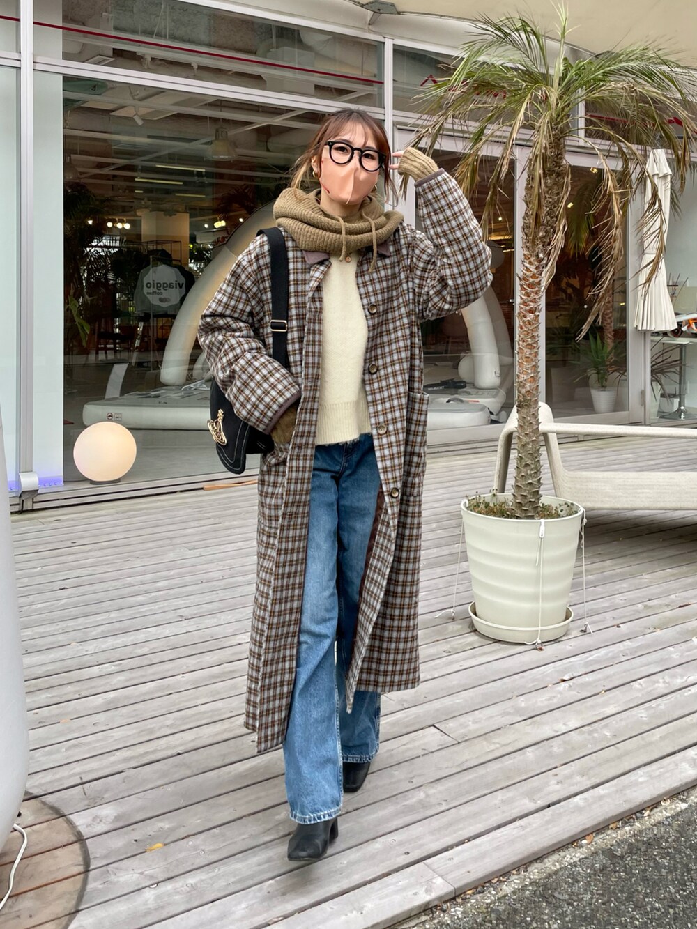 グレー系のステンカラーコート、ブルー系のデニムパンツ、ブラウン系のネックウォーマー/スヌードを着用したレディースの冬コーディネートの2枚目の写真