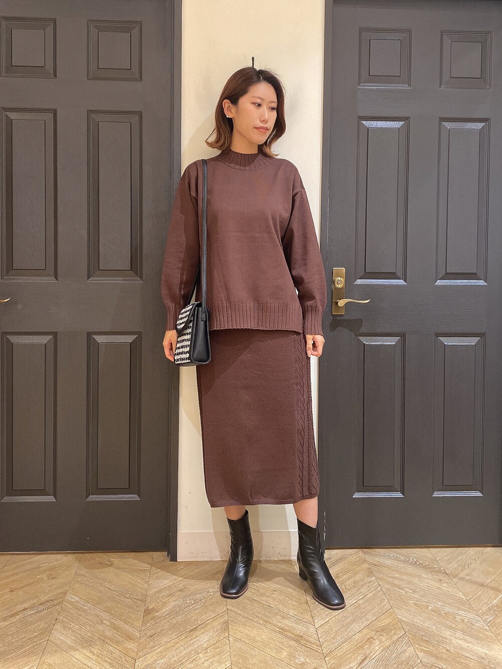 ブラウン系のスカート、ブラウン系のニット/セーター、ブラック系のショルダーバッグを着用したレディースの秋コーディネートの2枚目の写真
