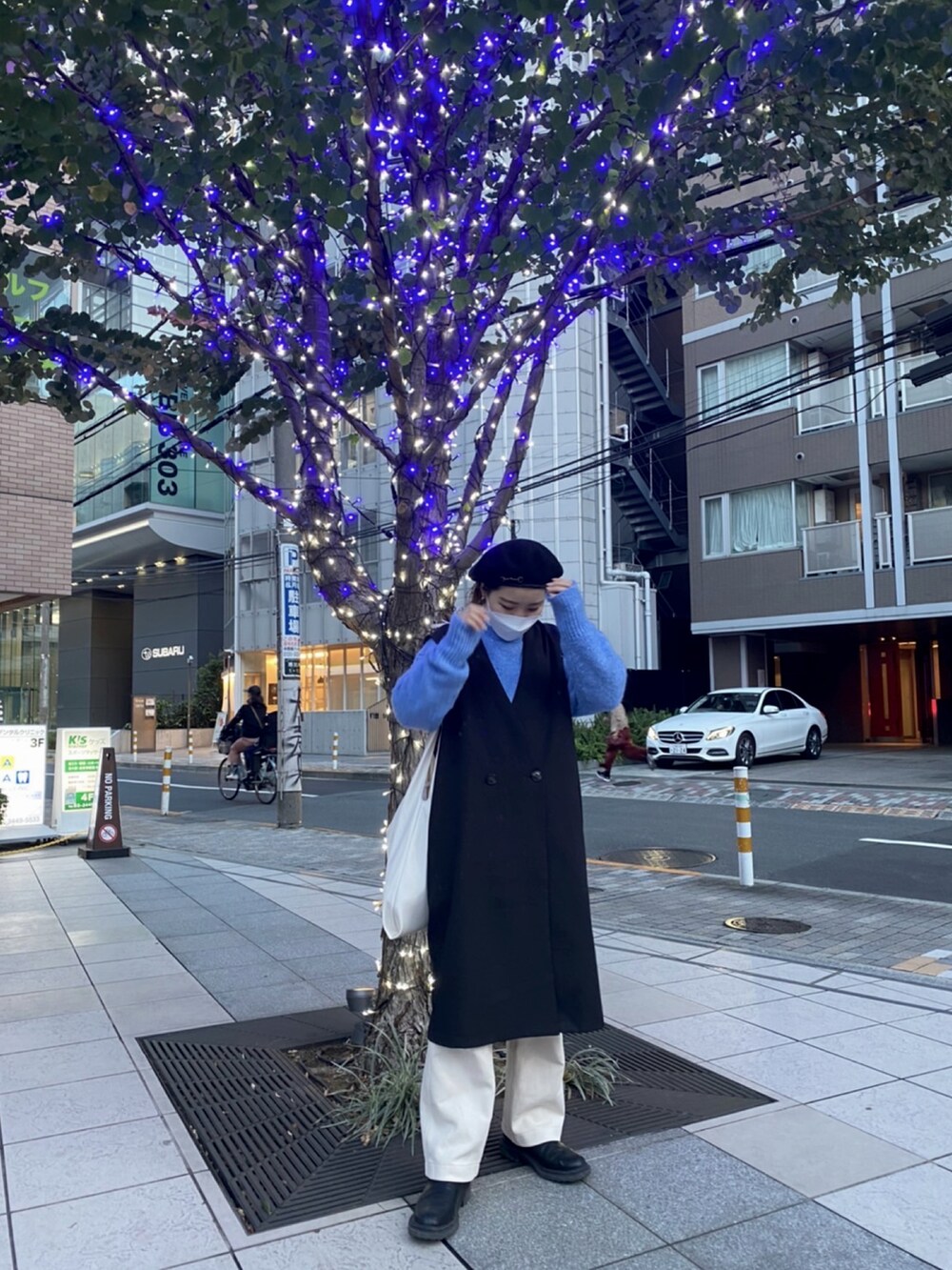 ホワイト系のトートバッグ、ブラック系のベスト、ブルー系のニット/セーターを着用したレディースの秋コーディネートの2枚目の写真