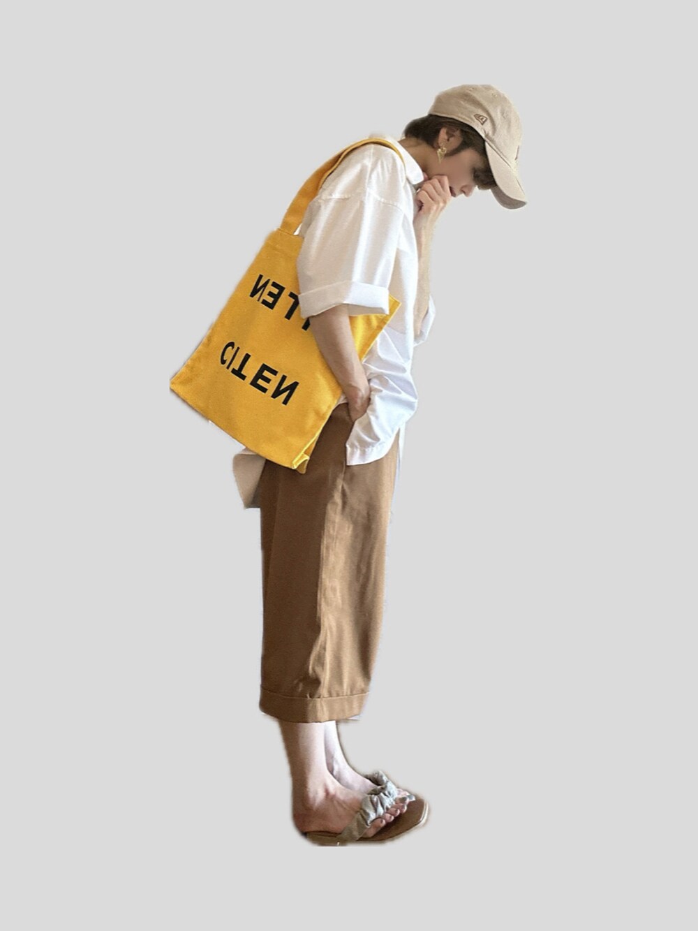 イエロー系のトートバッグ、ベージュ系のパンツ、ゴールド系のサンダルを着用したレディースの夏コーディネートの2枚目の写真