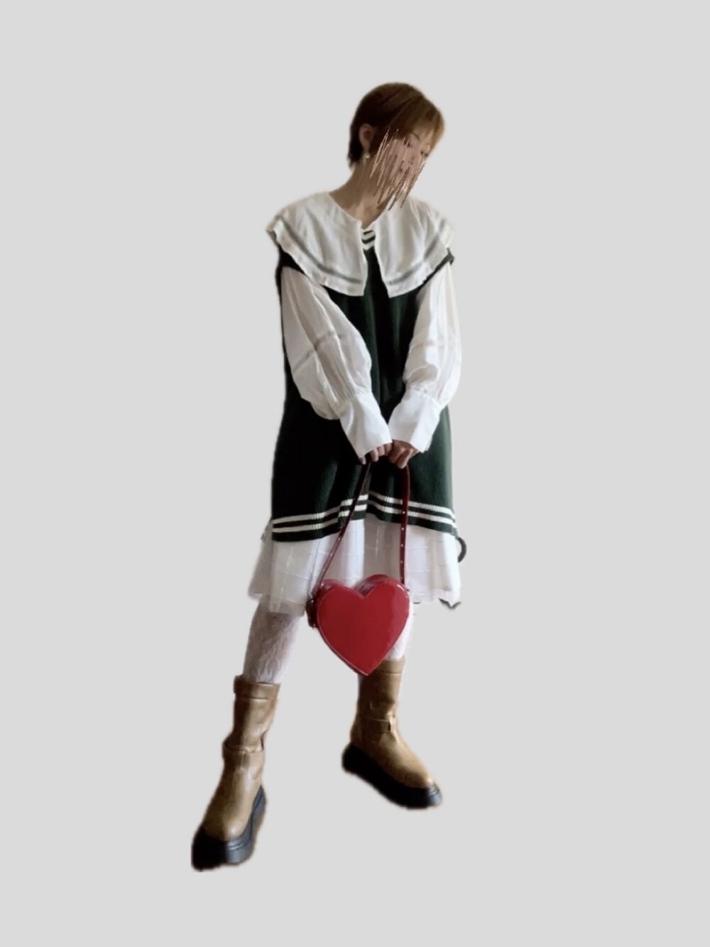 レッド系のハンドバッグ、ブラウン系のブーツ、グリーン系のベストを着用したレディースの秋コーディネートの3枚目の写真