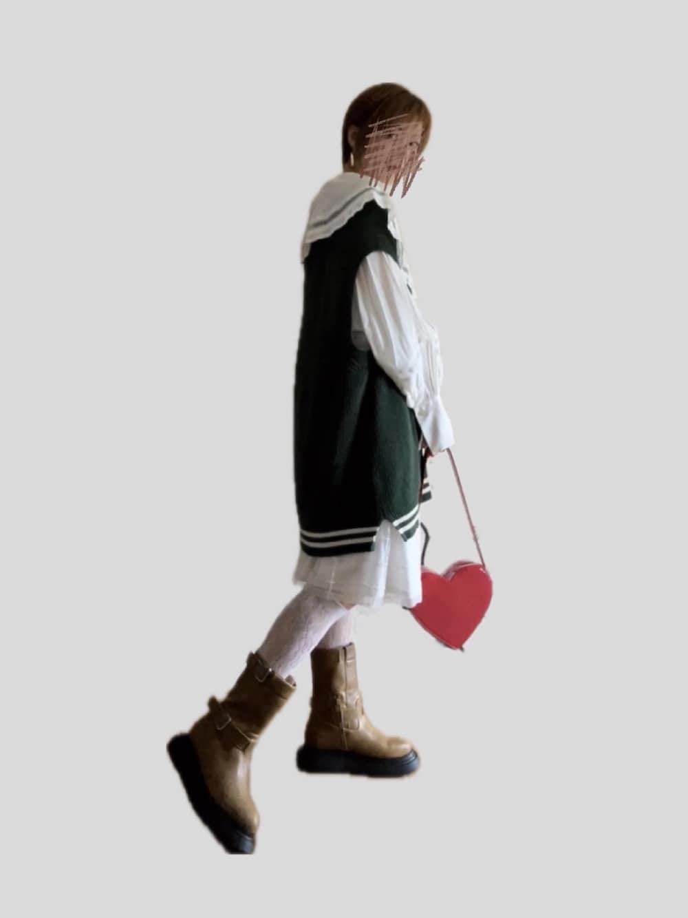 レッド系のハンドバッグ、ブラウン系のブーツ、グリーン系のベストを着用したレディースの秋コーディネートの2枚目の写真