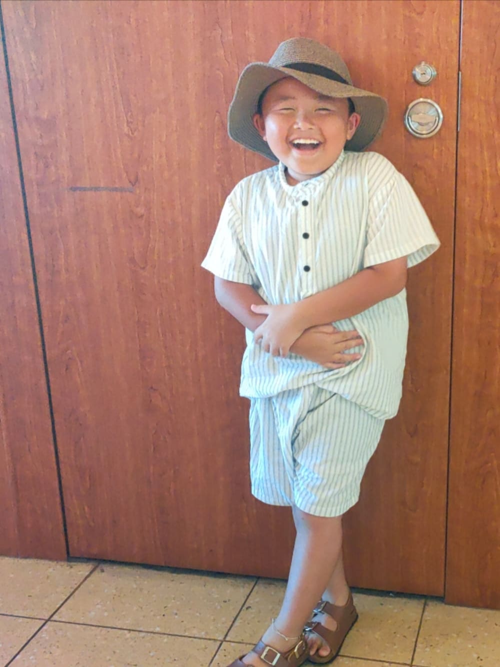 ホワイト系のセットアップ、ブラウン系のサンダル、ホワイト系のスーツケース/キャリーバッグを着用したキッズの夏コーディネートの3枚目の写真