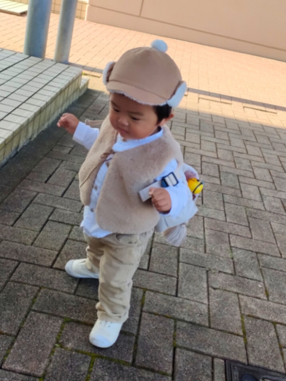 ベージュ系のベスト、ホワイト系のスニーカー、ベージュ系のパンツを着用したキッズの秋コーディネートの2枚目の写真