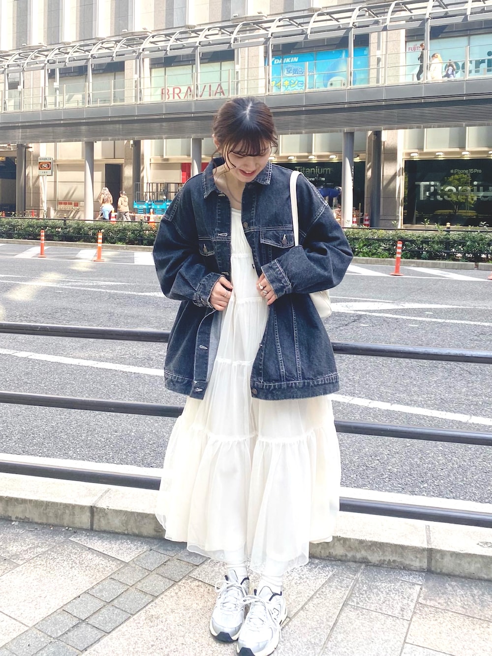 ブラック系のデニムジャケット、ホワイト系のワンピース、ホワイト系のショルダーバッグを着用したレディースの春コーディネートの2枚目の写真