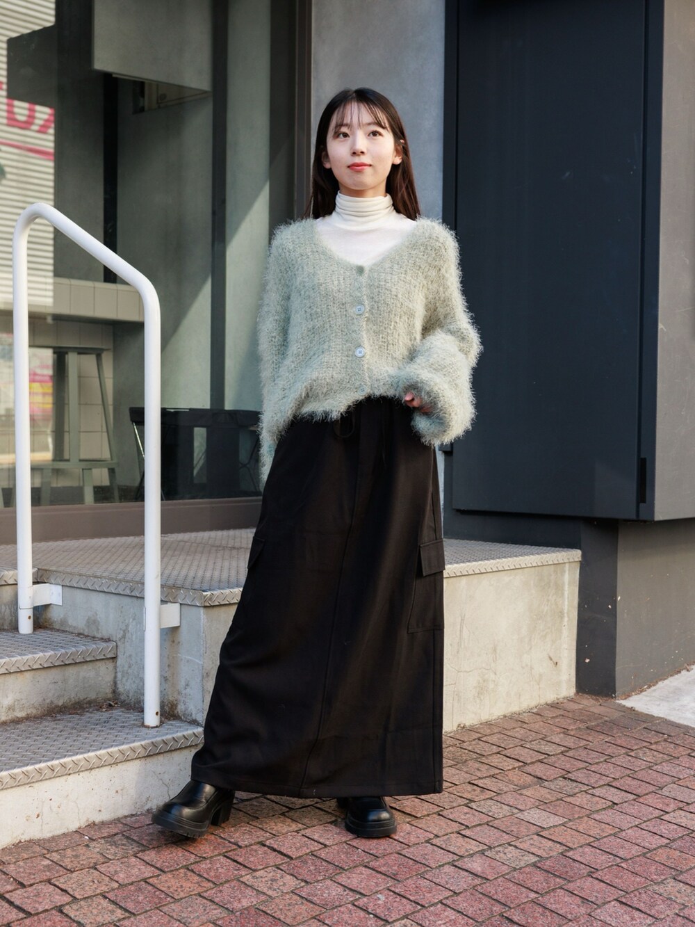 グリーン系のカーディガン/ボレロ、ベージュ系のTシャツ/カットソー、ブラック系のスカートを着用したレディースの冬コーディネートの2枚目の写真