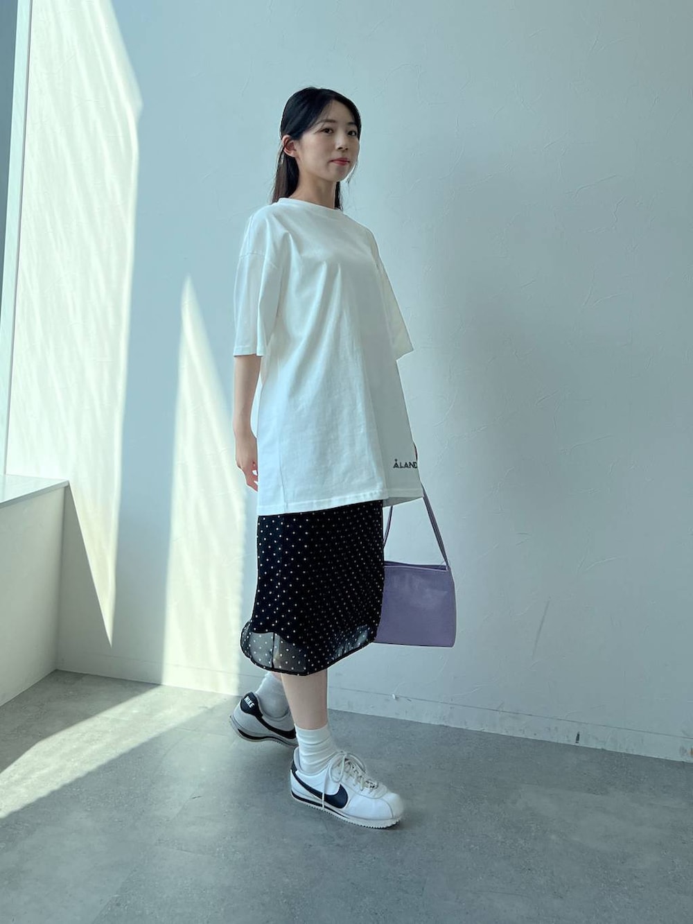 ブラック系のスカート、パープル系のハンドバッグ、ホワイト系のTシャツ/カットソーを着用したレディースの夏コーディネートの2枚目の写真