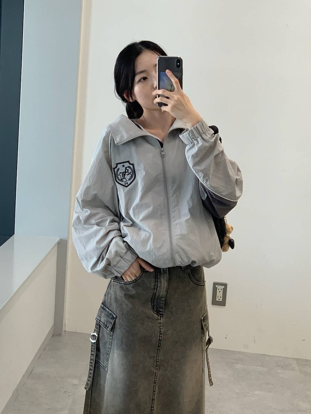 グレー系のナイロンジャケット、ブラック系のデニムスカート、ブラック系のショルダーバッグを着用したレディースの夏コーディネートの4枚目の写真