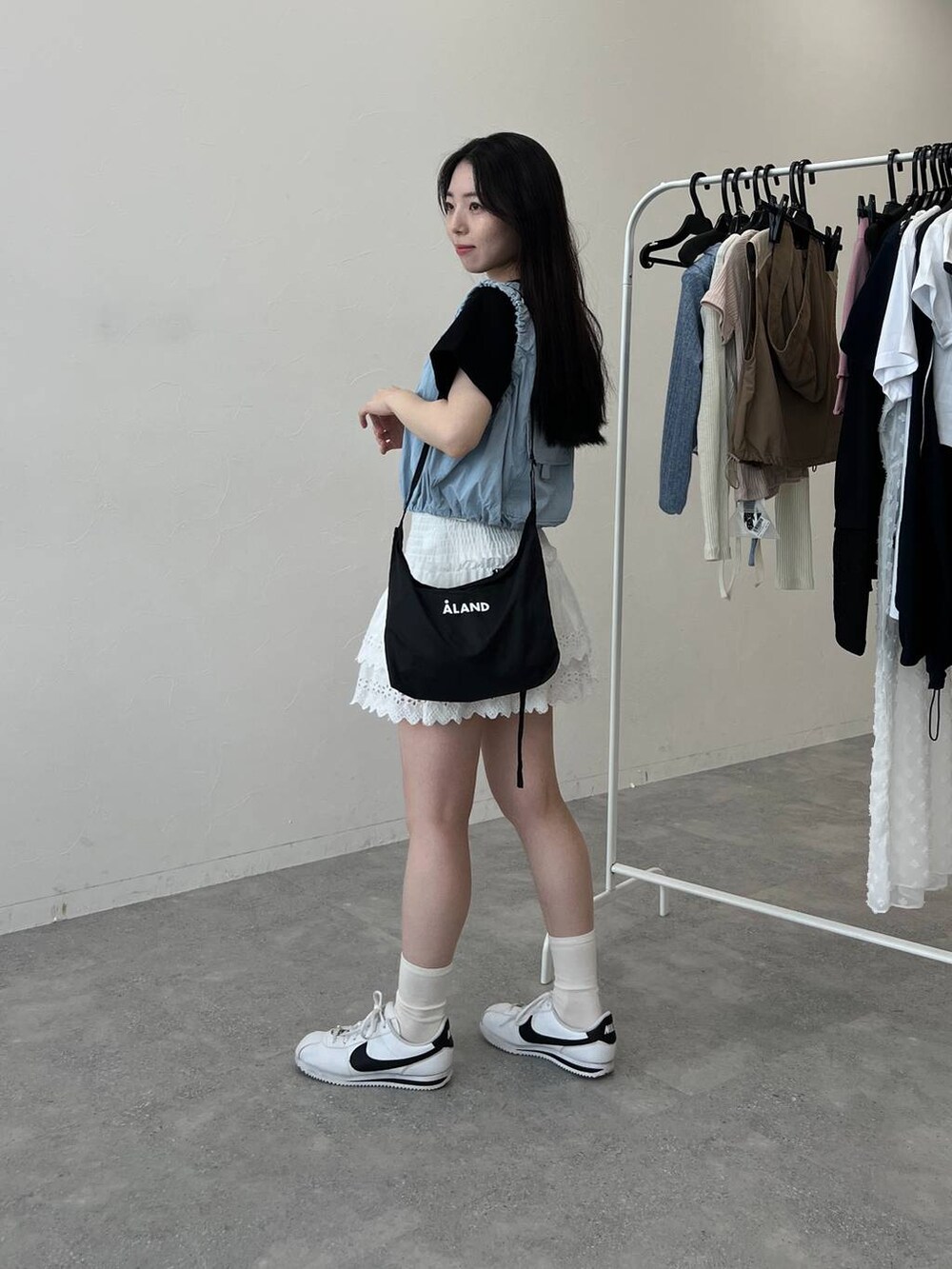 ブルー系のベスト、ホワイト系のスカート、ブラック系のショルダーバッグを着用したレディースの夏コーディネートの4枚目の写真