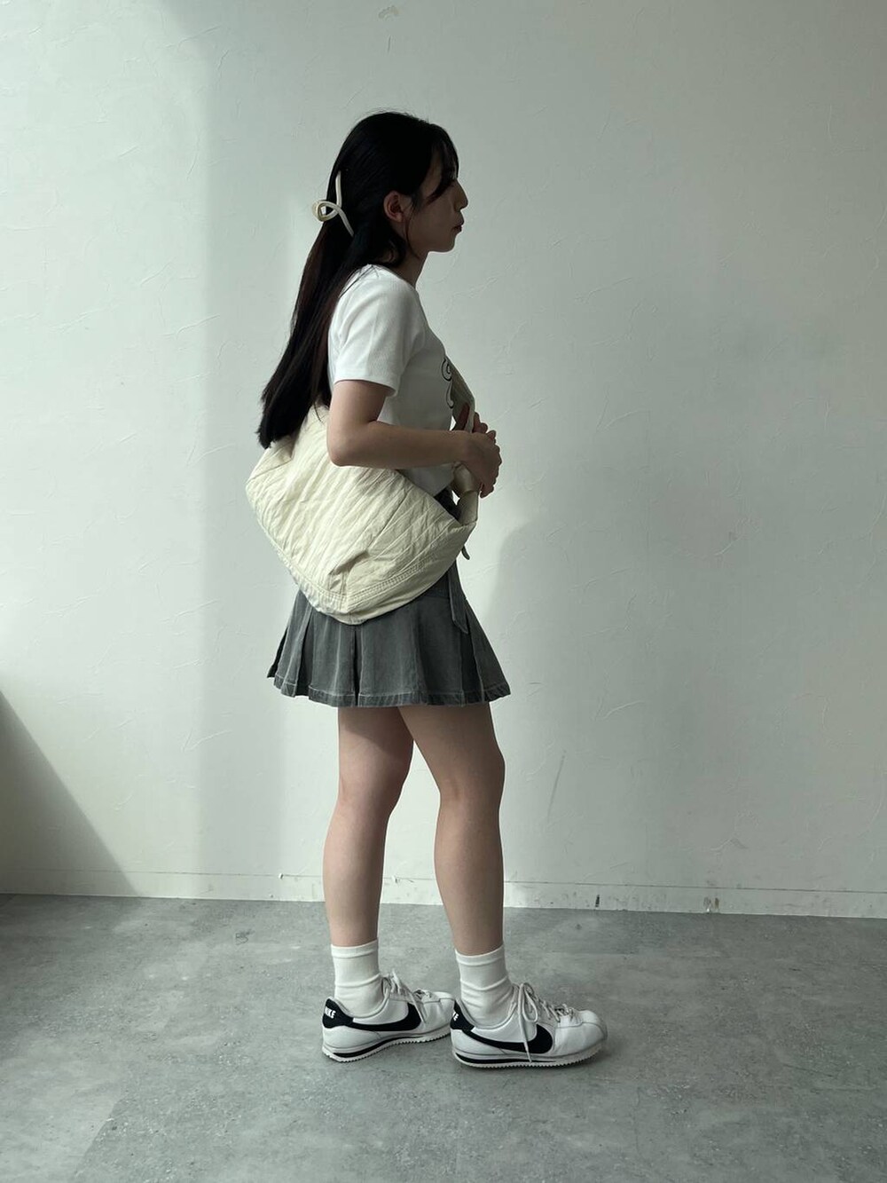 ベージュ系のショルダーバッグ、ホワイト系のTシャツ/カットソー、グレー系のデニムスカートを着用したレディースの夏コーディネートの3枚目の写真