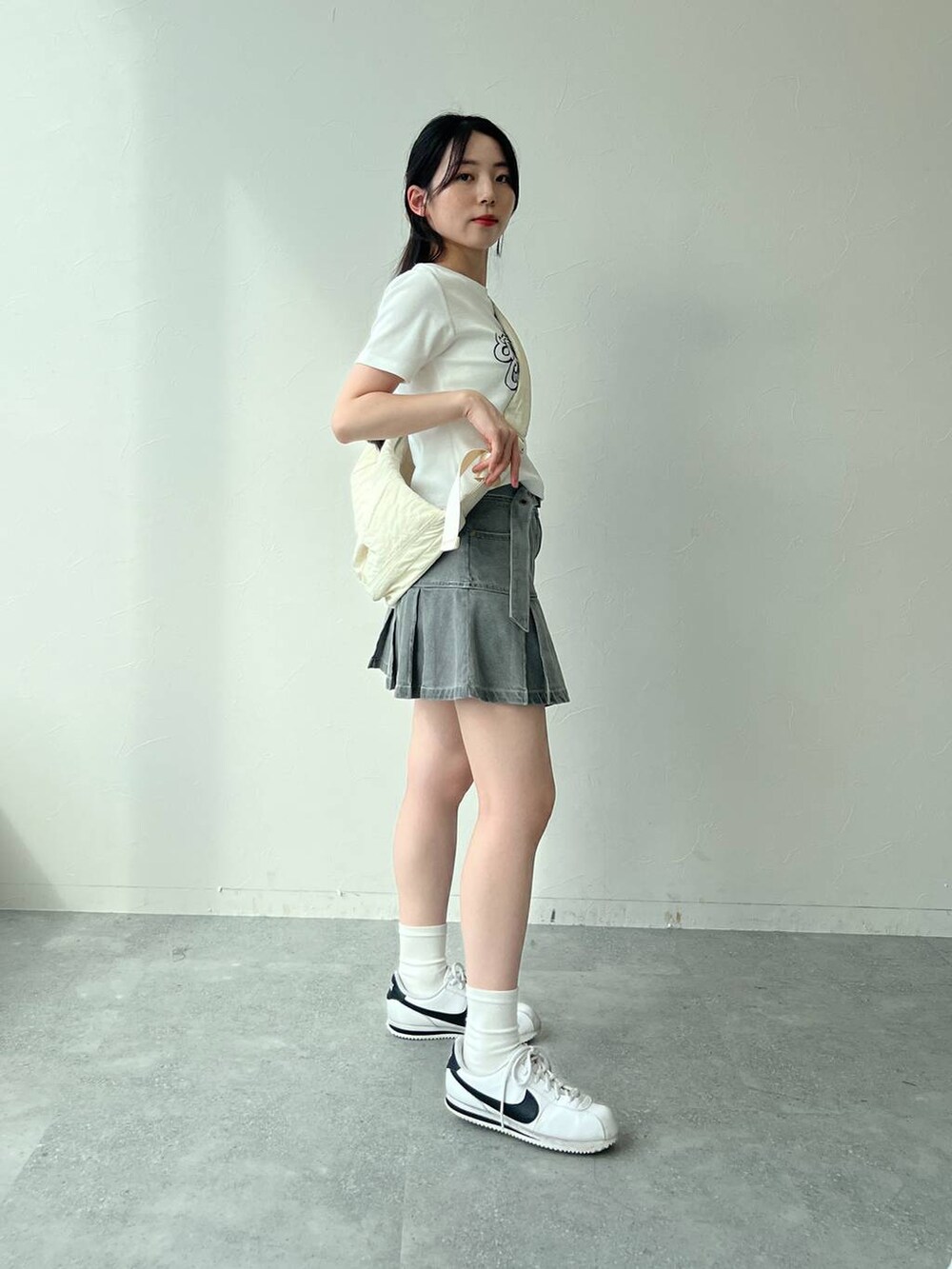 ベージュ系のショルダーバッグ、ホワイト系のTシャツ/カットソー、グレー系のデニムスカートを着用したレディースの夏コーディネートの2枚目の写真