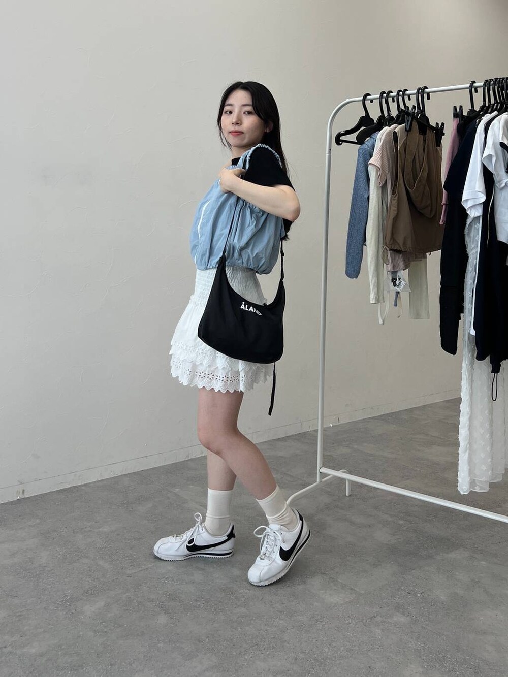 ブルー系のベスト、ホワイト系のスカート、ブラック系のショルダーバッグを着用したレディースの夏コーディネートの2枚目の写真