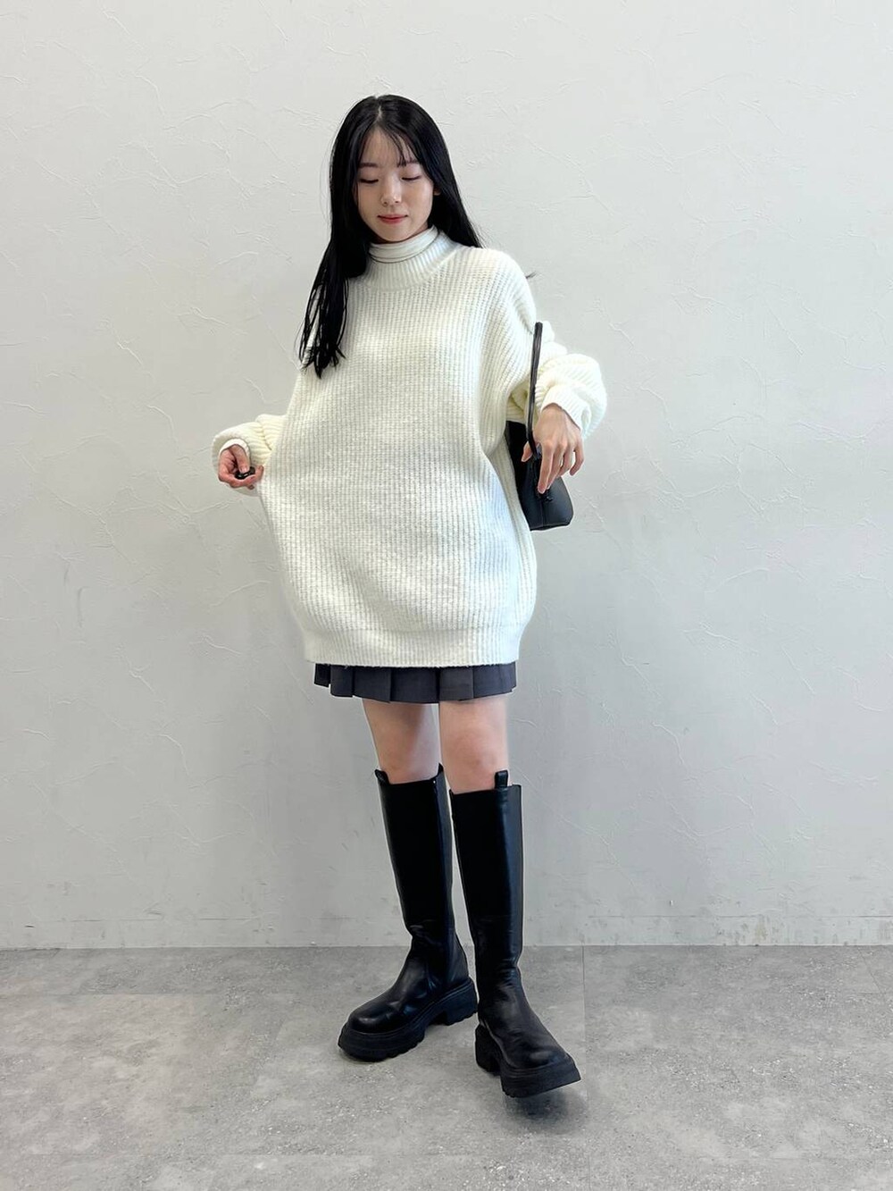 ブラック系のブーツ、ブラック系のショルダーバッグ、ホワイト系のニット/セーターを着用したレディースの冬コーディネートの2枚目の写真