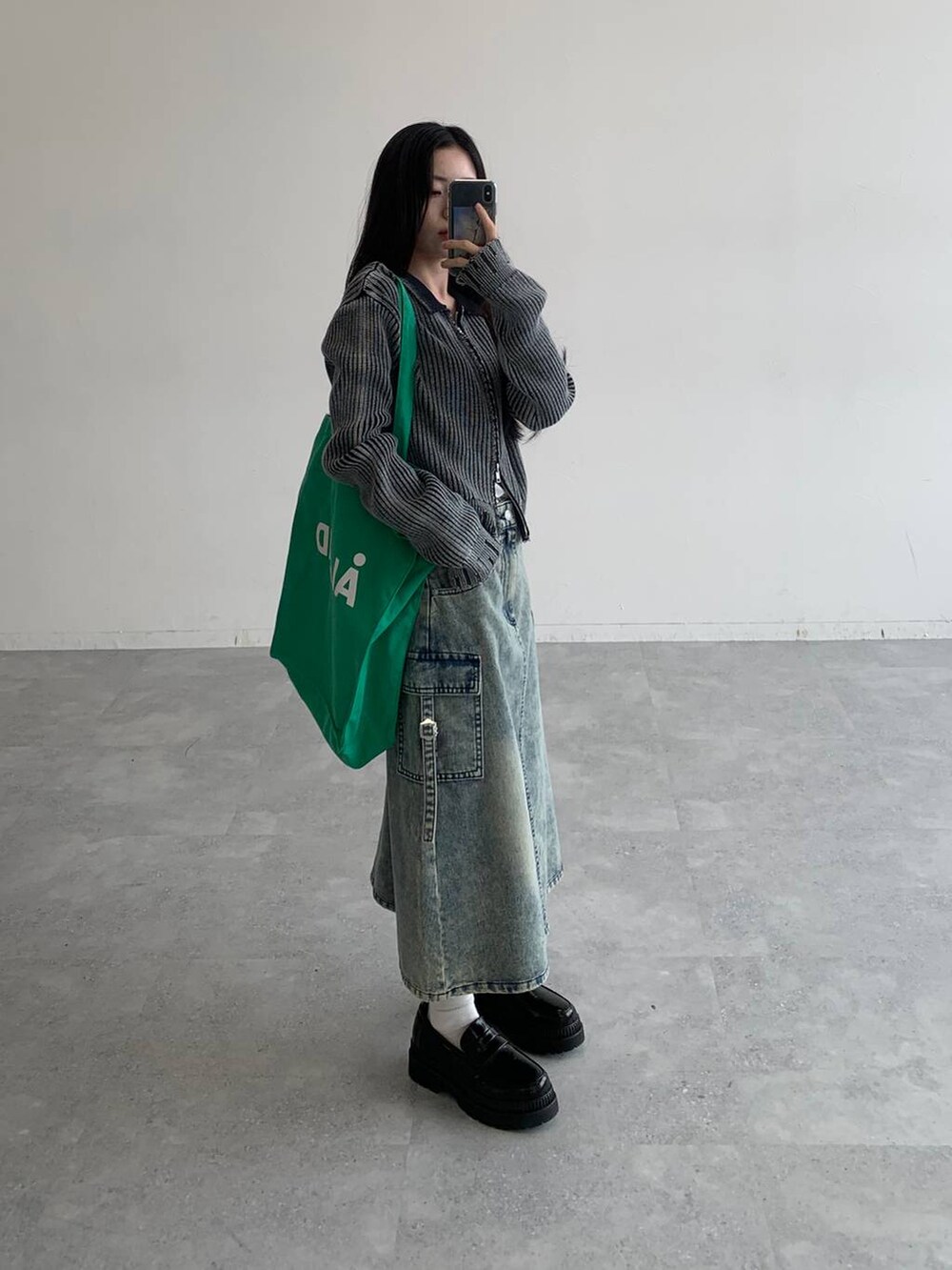 ブルー系のデニムスカート、グリーン系のトートバッグ、ブラック系のニット/セーターを着用したレディースの秋コーディネートの2枚目の写真