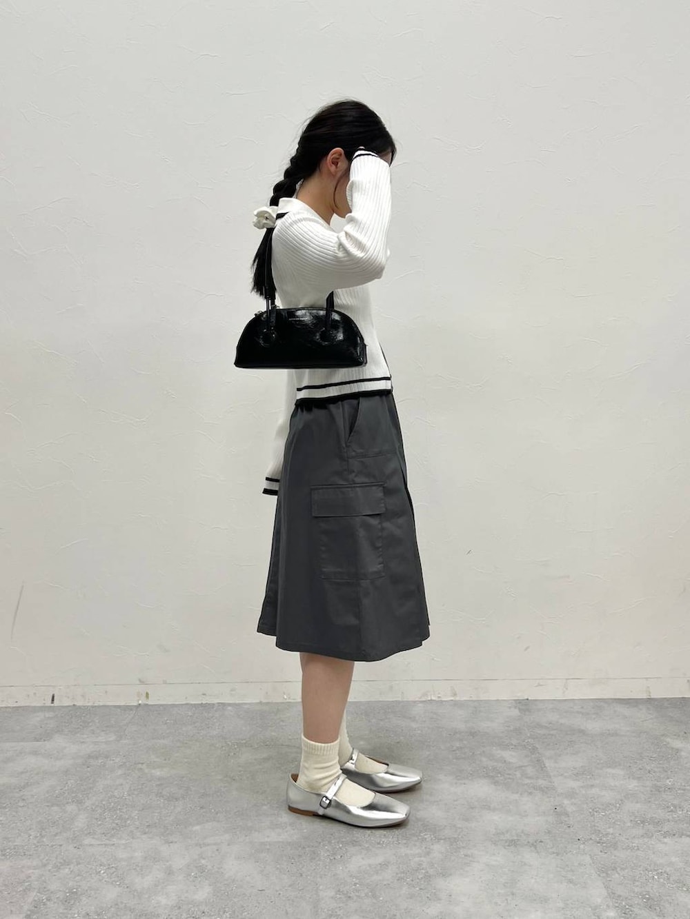 グレー系のスカート、ホワイト系のカーディガン/ボレロ、ブラック系のハンドバッグを着用したレディースの冬コーディネートの3枚目の写真