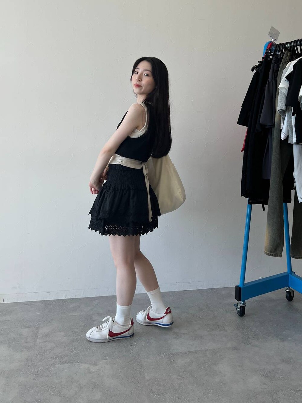 ブラック系のスカート、ブラック系のベスト、ベージュ系のショルダーバッグを着用したレディースの春コーディネートの2枚目の写真