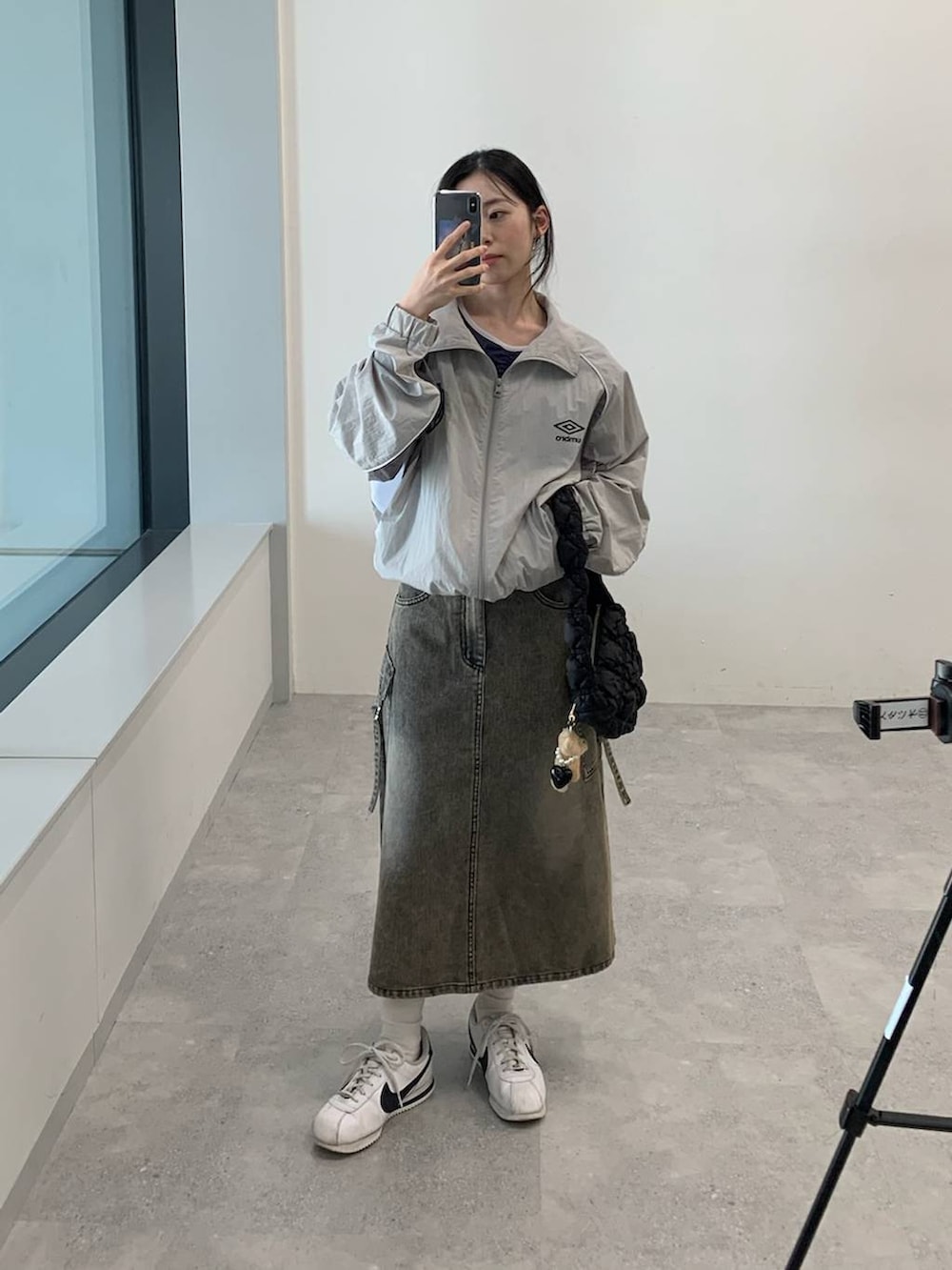 グレー系のナイロンジャケット、ブラック系のデニムスカート、ブラック系のショルダーバッグを着用したレディースの夏コーディネートの2枚目の写真