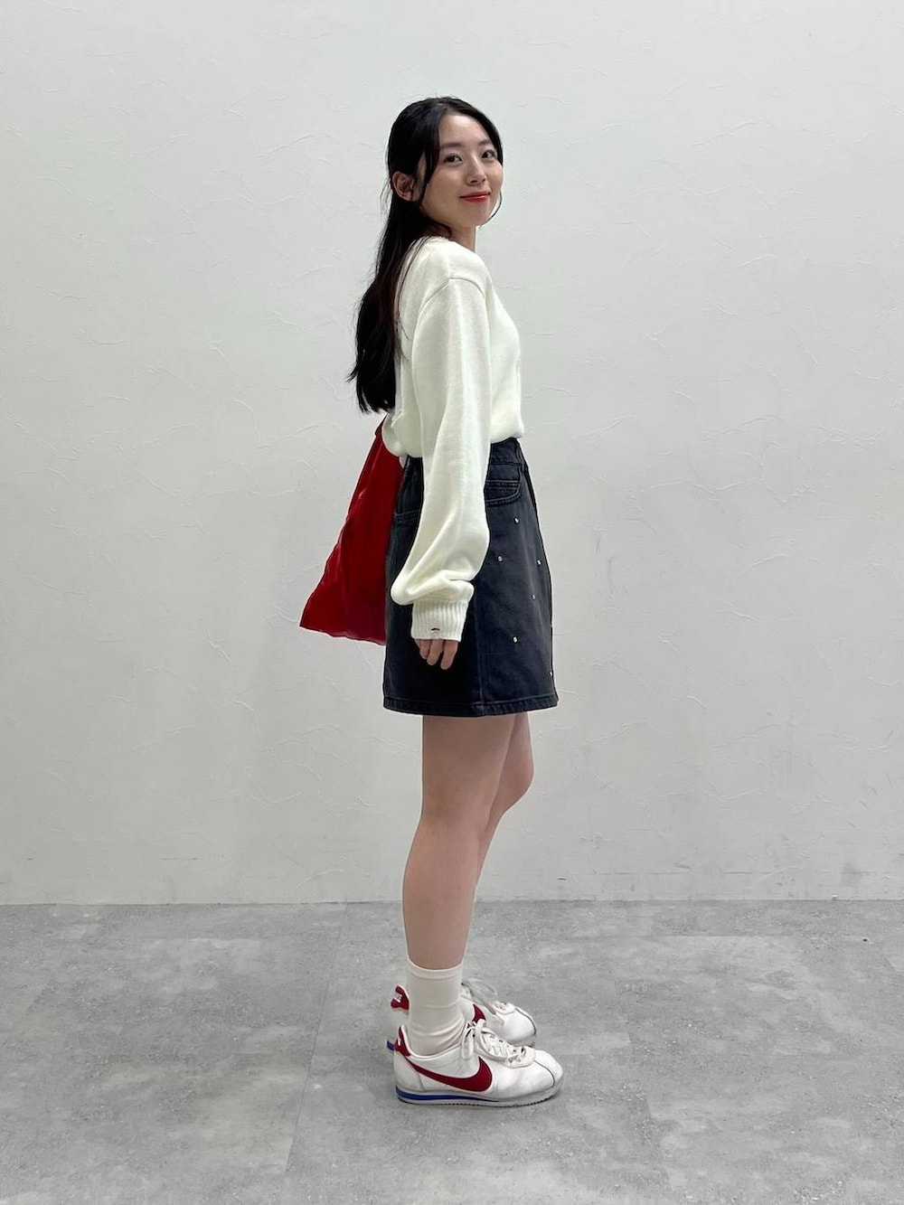 ホワイト系のニット/セーター、レッド系のトートバッグ、ブラック系のデニムスカートを着用したレディースの春コーディネートの6枚目の写真