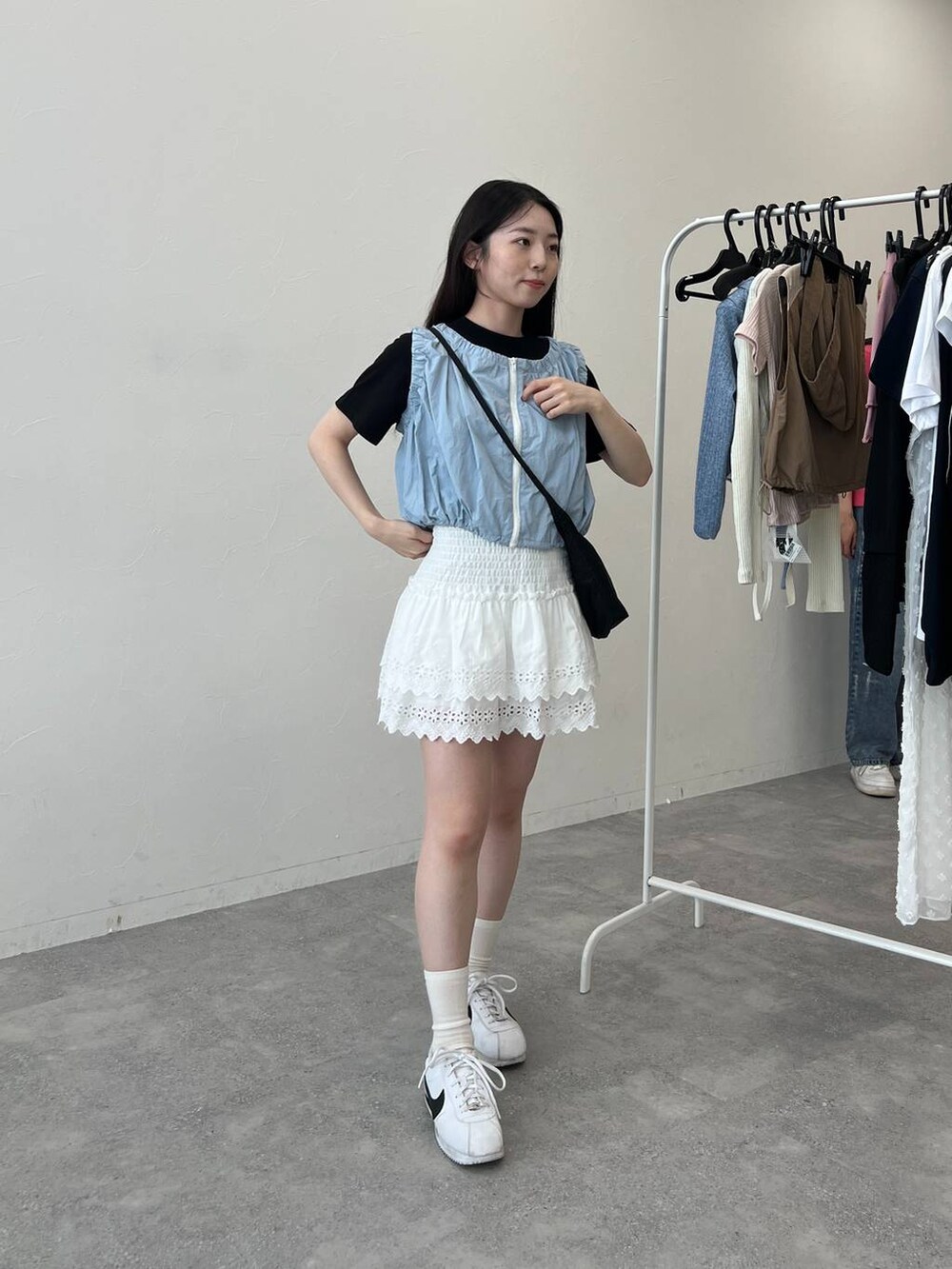 ブルー系のベスト、ホワイト系のスカート、ブラック系のショルダーバッグを着用したレディースの夏コーディネートの6枚目の写真