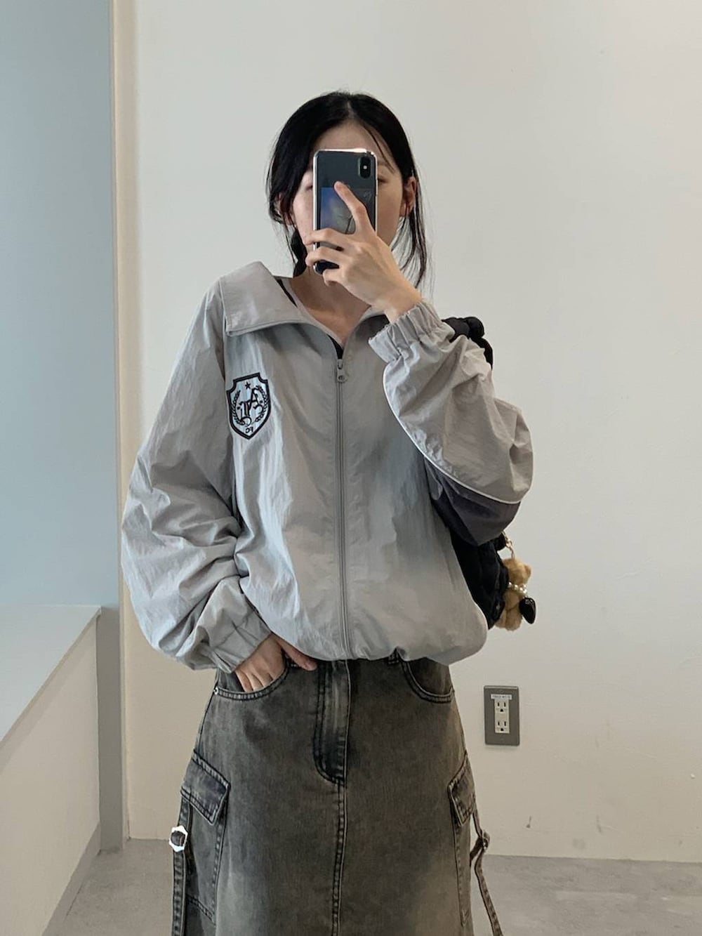 グレー系のナイロンジャケット、ブラック系のデニムスカート、ブラック系のショルダーバッグを着用したレディースの夏コーディネートの3枚目の写真