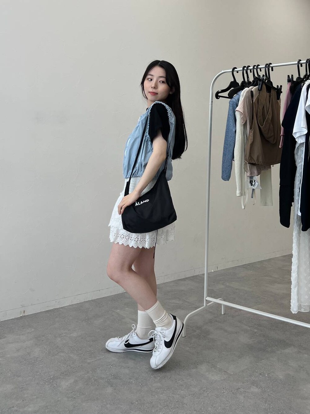 ブルー系のベスト、ホワイト系のスカート、ブラック系のショルダーバッグを着用したレディースの夏コーディネートの3枚目の写真