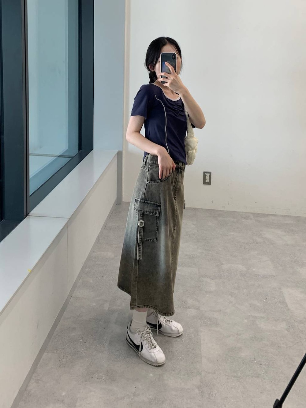 ブラック系のデニムスカート、ホワイト系のショルダーバッグ、ブルー系のTシャツ/カットソーを着用したレディースの夏コーディネートの5枚目の写真