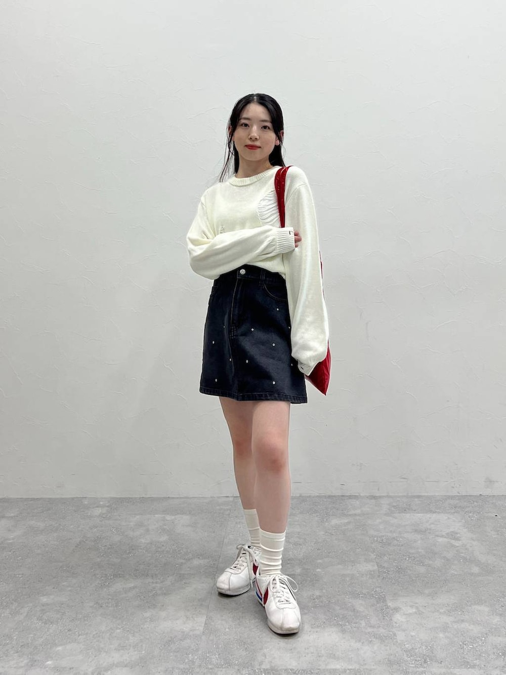 ホワイト系のニット/セーター、レッド系のトートバッグ、ブラック系のデニムスカートを着用したレディースの春コーディネートの2枚目の写真