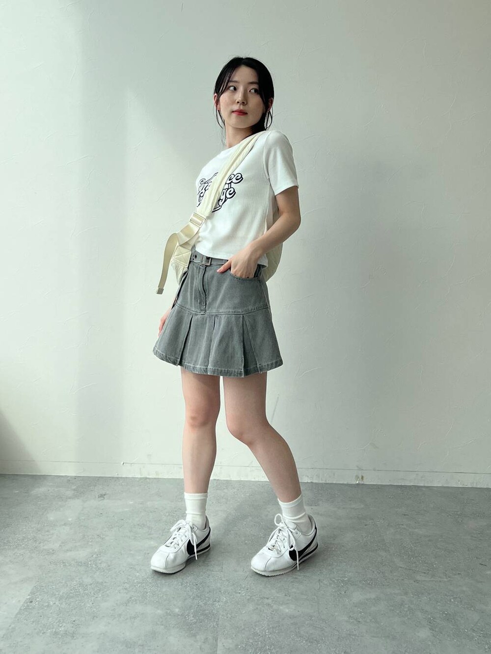 ベージュ系のショルダーバッグ、ホワイト系のTシャツ/カットソー、グレー系のデニムスカートを着用したレディースの夏コーディネートの6枚目の写真