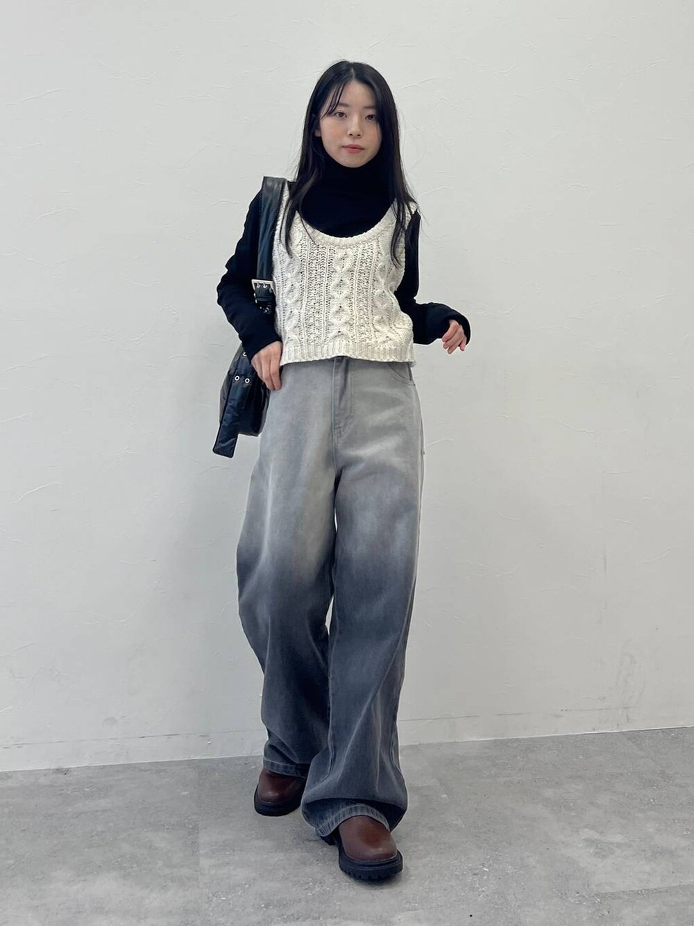 ブラック系のショルダーバッグ、ブラック系のデニムパンツ、ベージュ系のベストを着用したレディースの冬コーディネートの2枚目の写真