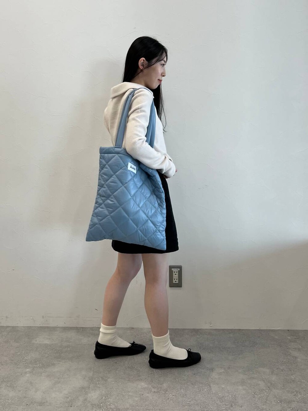 ブラック系のデニムスカート、ブラック系のバレエシューズ、ブルー系のトートバッグを着用したレディースの冬コーディネートの5枚目の写真