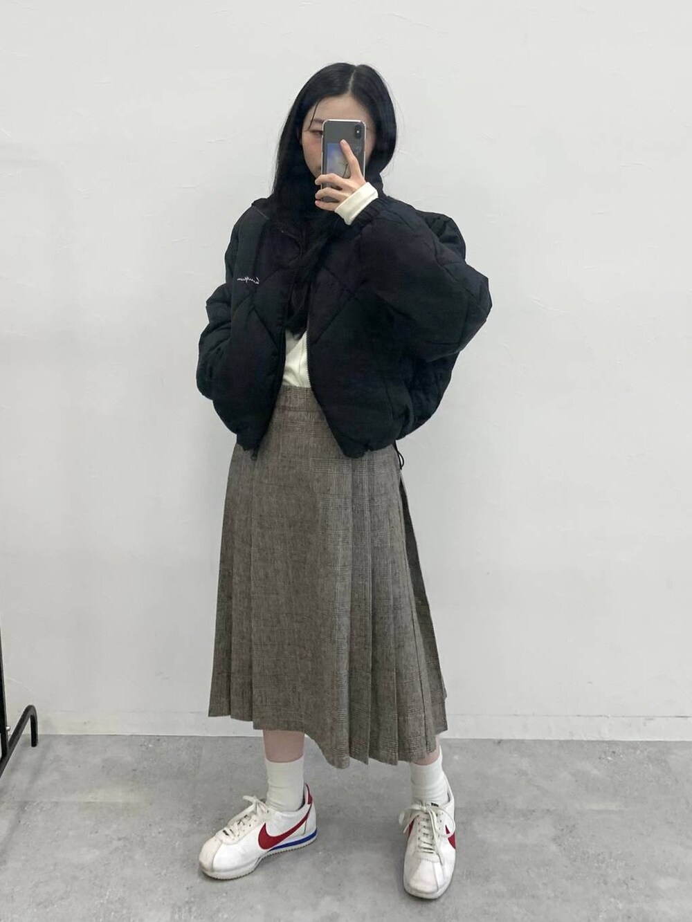 ブラウン系のスカート、ベージュ系のTシャツ/カットソー、ブラック系のダウンジャケット/コートを着用したレディースの冬コーディネートの3枚目の写真