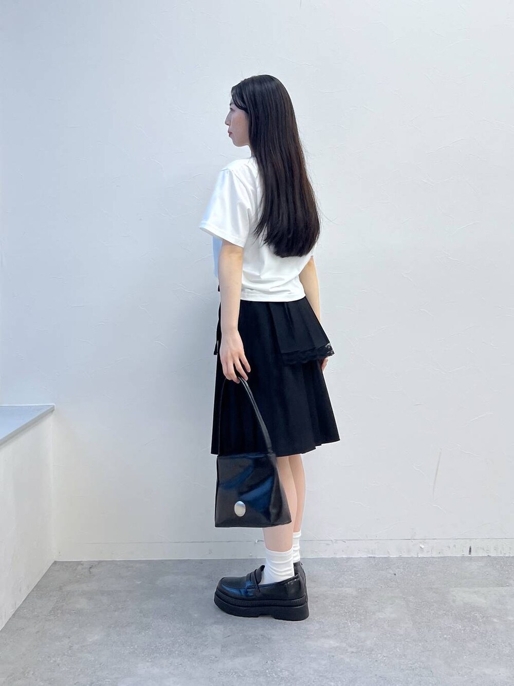 ブラック系のスカート、ホワイト系のTシャツ/カットソー、ブラック系のハンドバッグを着用したレディースの夏コーディネートの3枚目の写真