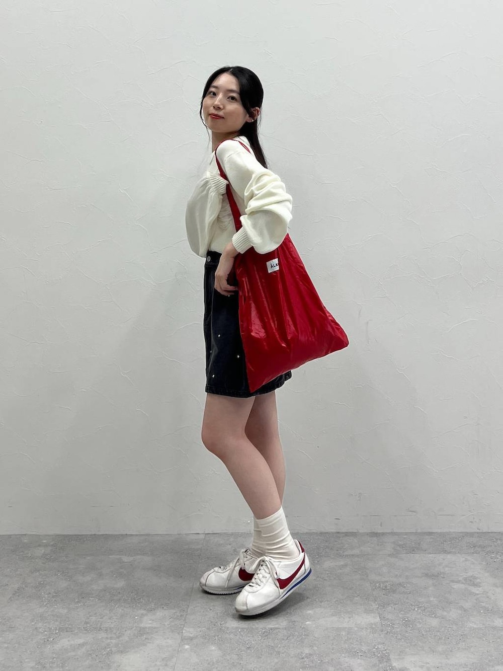 ホワイト系のニット/セーター、レッド系のトートバッグ、ブラック系のデニムスカートを着用したレディースの春コーディネートの4枚目の写真