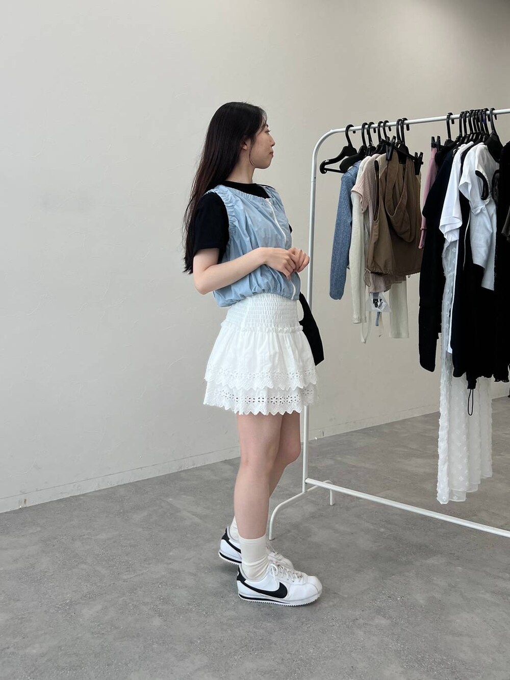 ブルー系のベスト、ホワイト系のスカート、ブラック系のショルダーバッグを着用したレディースの夏コーディネートの5枚目の写真