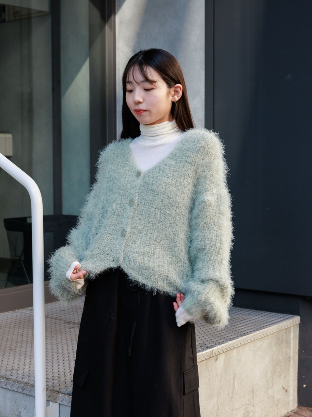グリーン系のカーディガン/ボレロ、ベージュ系のTシャツ/カットソー、ブラック系のスカートを着用したレディースの冬コーディネートの4枚目の写真