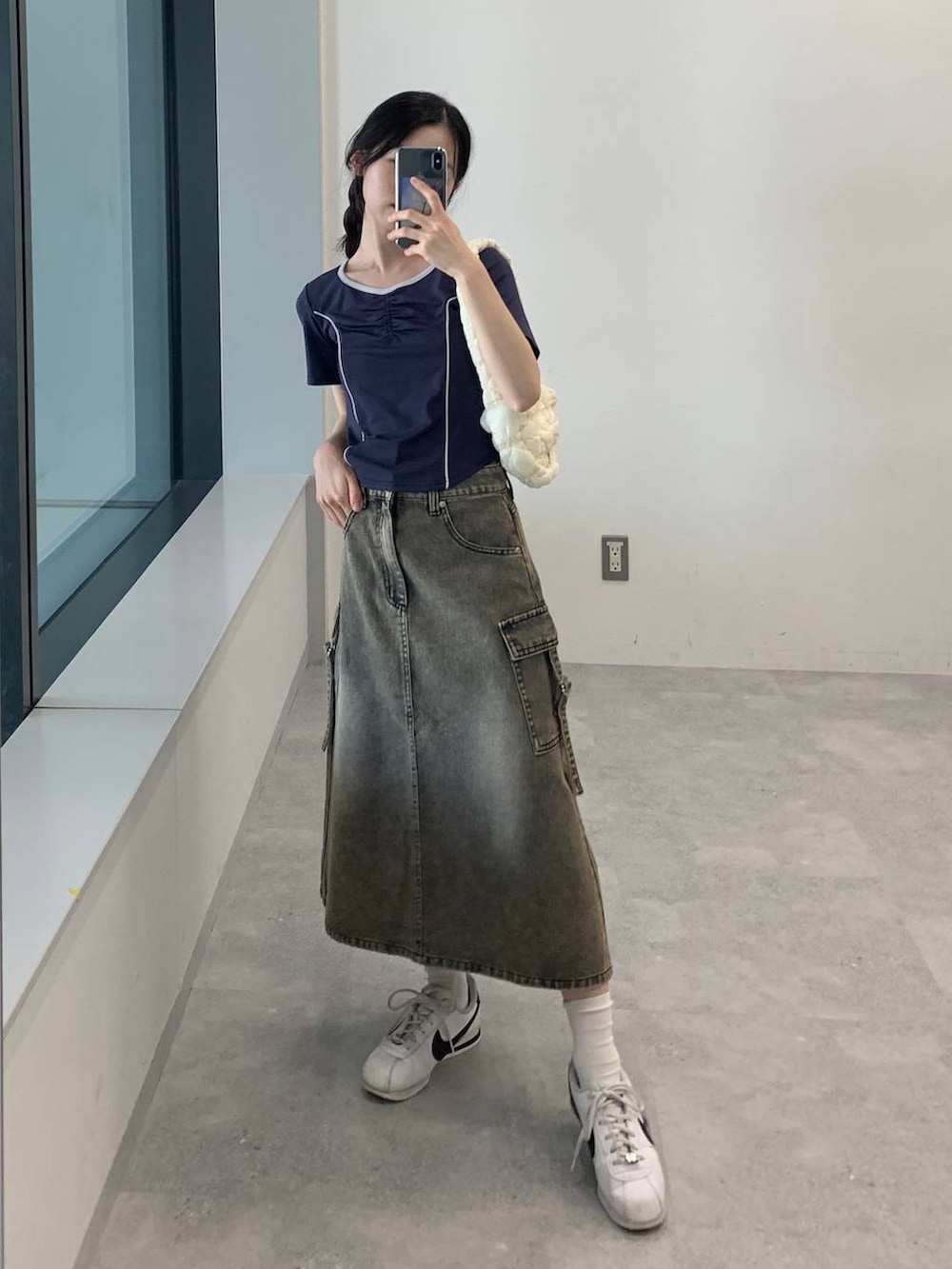 ブラック系のデニムスカート、ホワイト系のショルダーバッグ、ブルー系のTシャツ/カットソーを着用したレディースの夏コーディネートの2枚目の写真