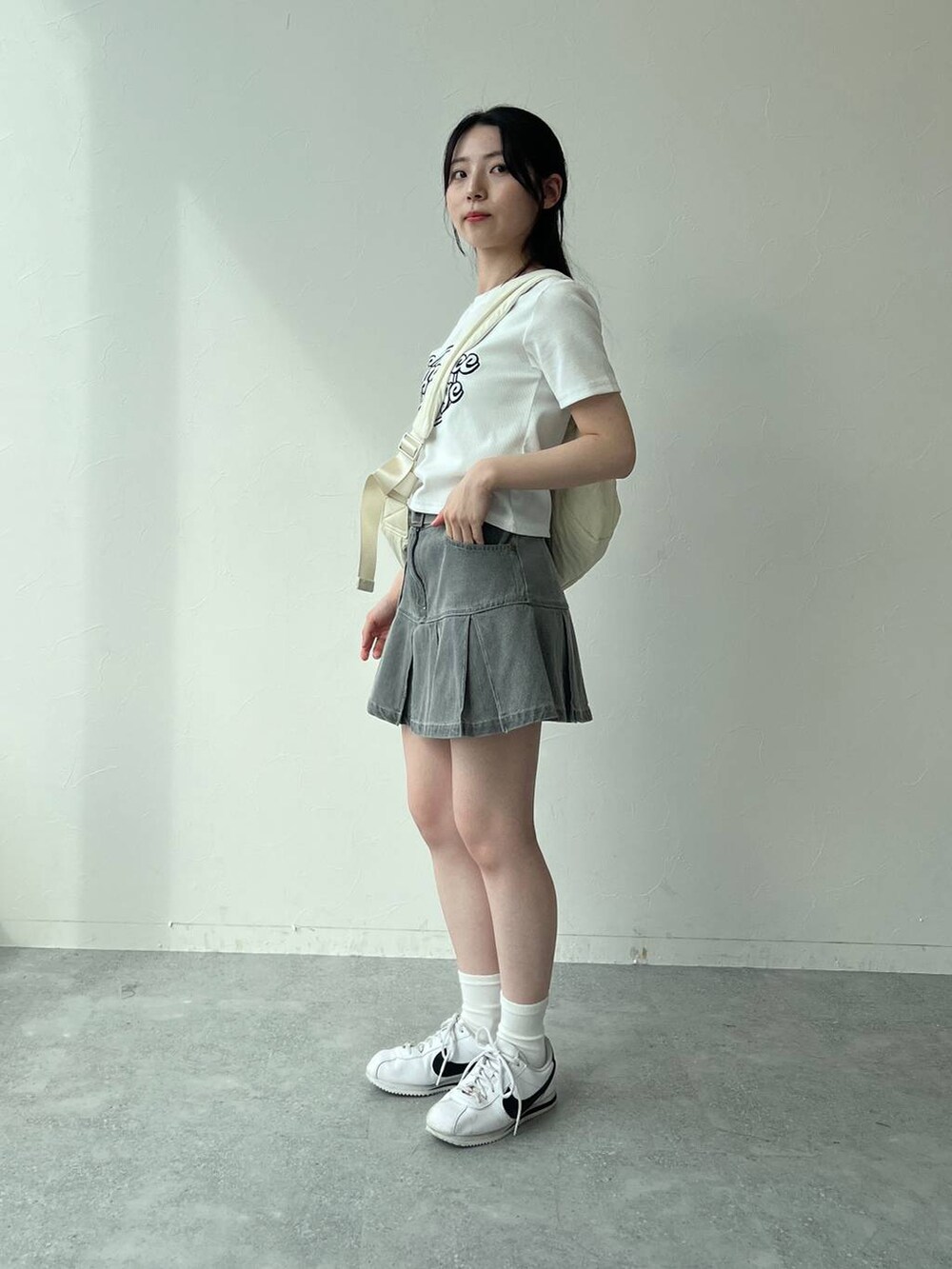 ベージュ系のショルダーバッグ、ホワイト系のTシャツ/カットソー、グレー系のデニムスカートを着用したレディースの夏コーディネートの5枚目の写真