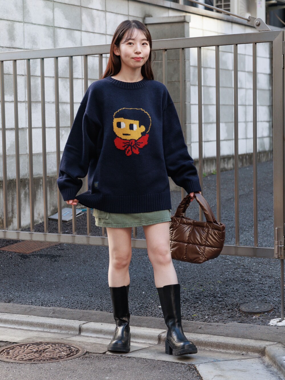 ブラック系のブーツ、ブラウン系のハンドバッグ、グリーン系のスカートを着用したレディースの冬コーディネートの2枚目の写真