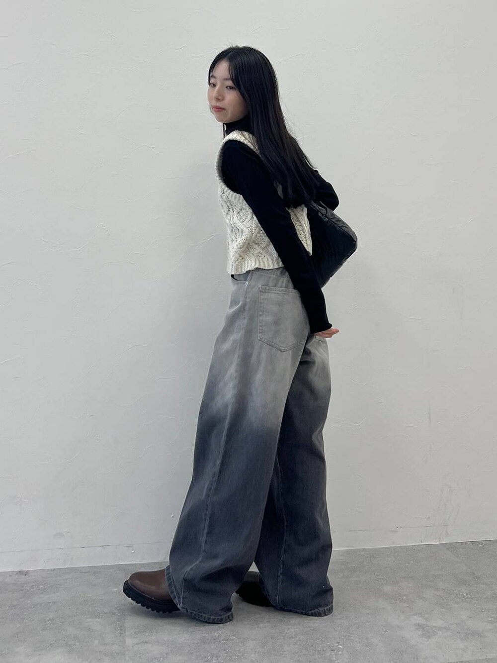 ブラック系のショルダーバッグ、ブラック系のデニムパンツ、ベージュ系のベストを着用したレディースの冬コーディネートの3枚目の写真