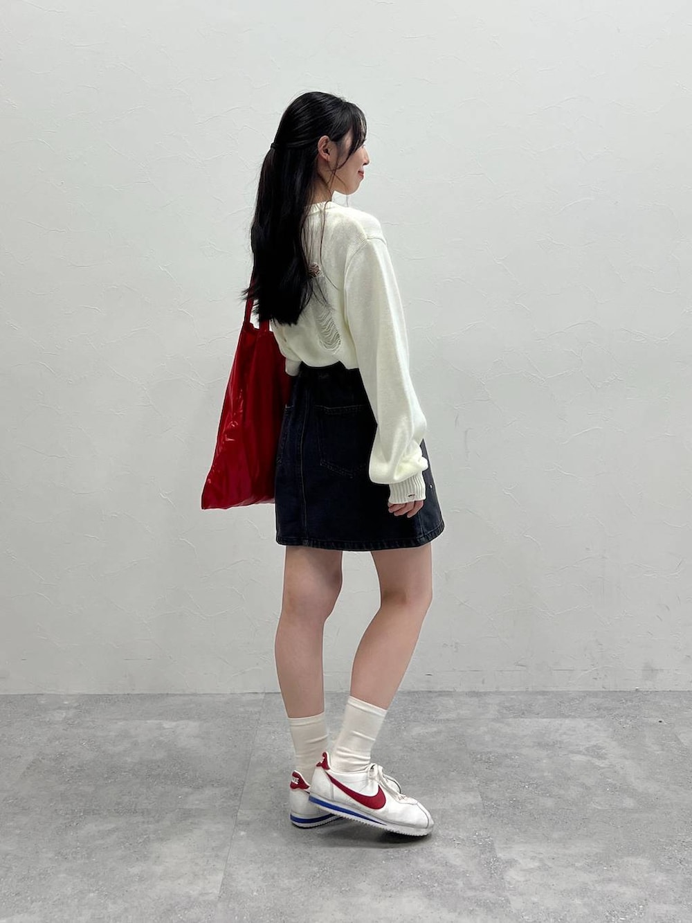 ホワイト系のニット/セーター、レッド系のトートバッグ、ブラック系のデニムスカートを着用したレディースの春コーディネートの5枚目の写真