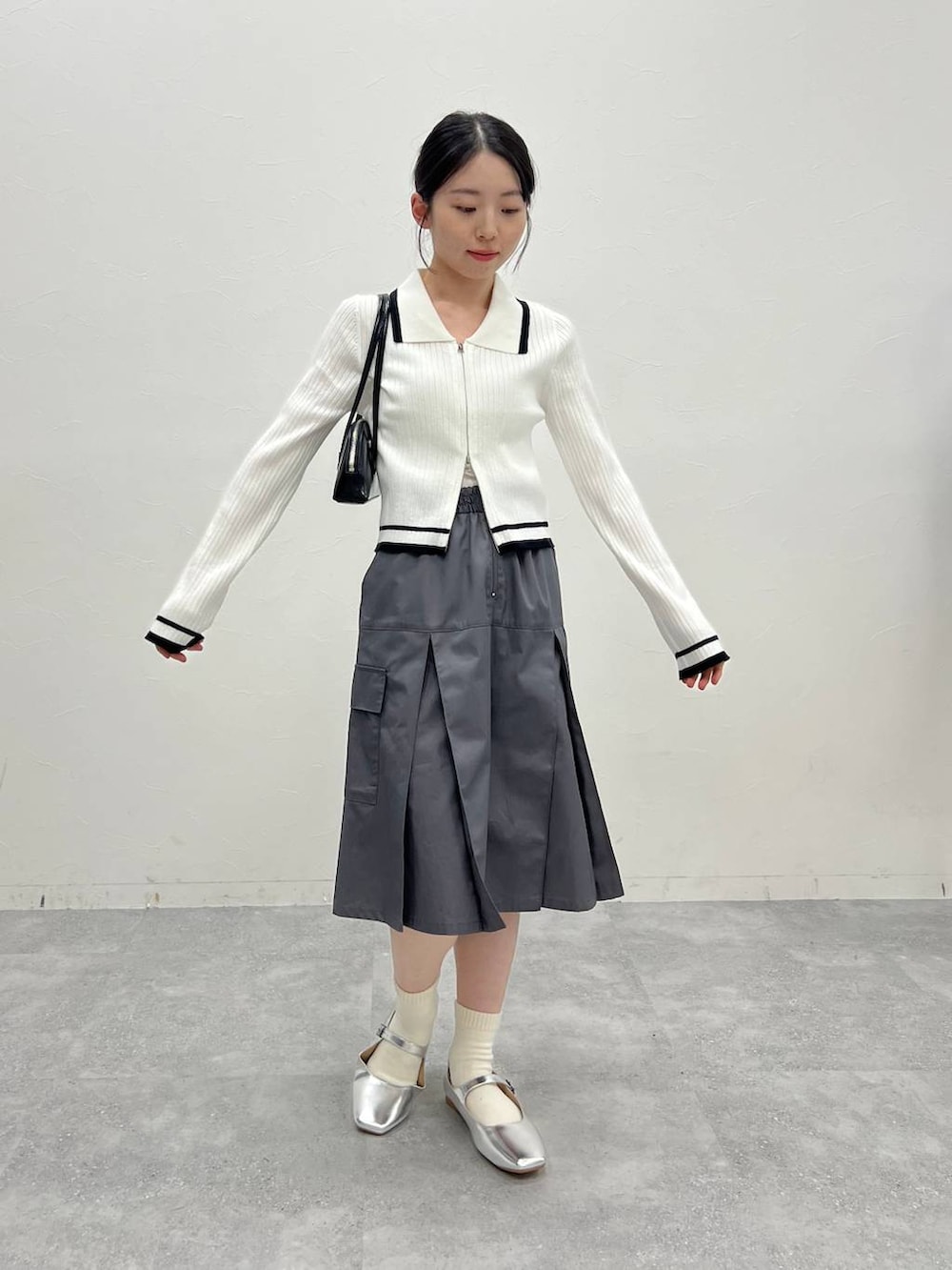 グレー系のスカート、ホワイト系のカーディガン/ボレロ、ブラック系のハンドバッグを着用したレディースの冬コーディネートの2枚目の写真