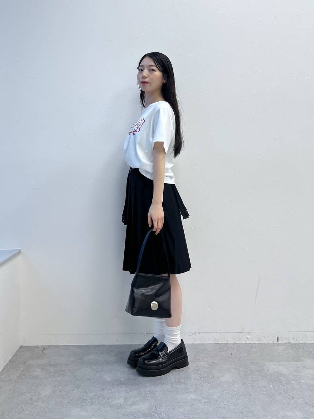 ブラック系のスカート、ホワイト系のTシャツ/カットソー、ブラック系のハンドバッグを着用したレディースの夏コーディネートの2枚目の写真