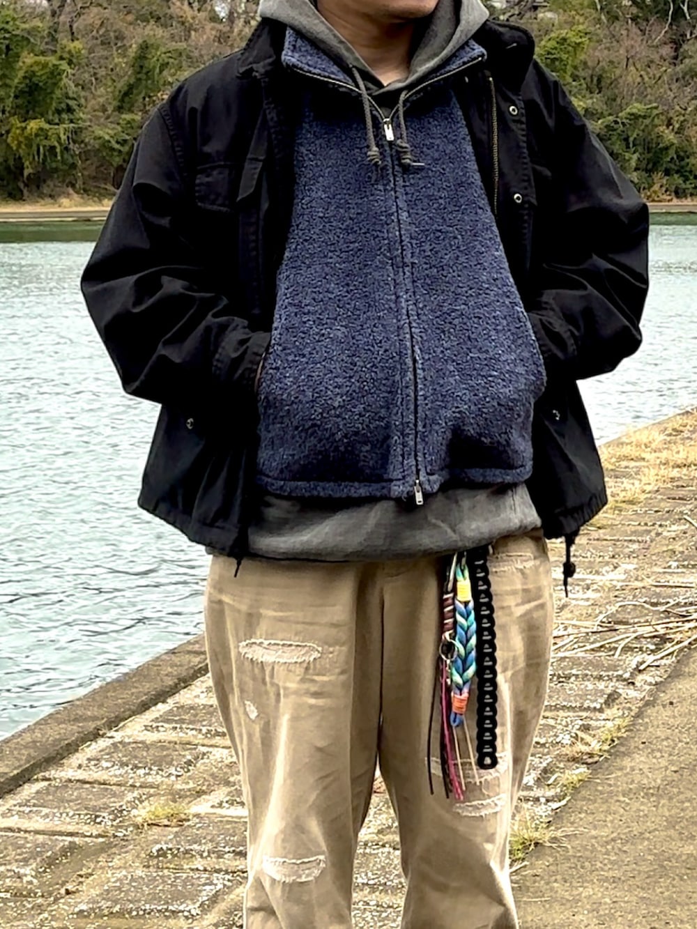 ブラック系のブーツ、ベージュ系のチノパンツ、ブルー系のベストを着用したメンズの冬コーディネートの2枚目の写真