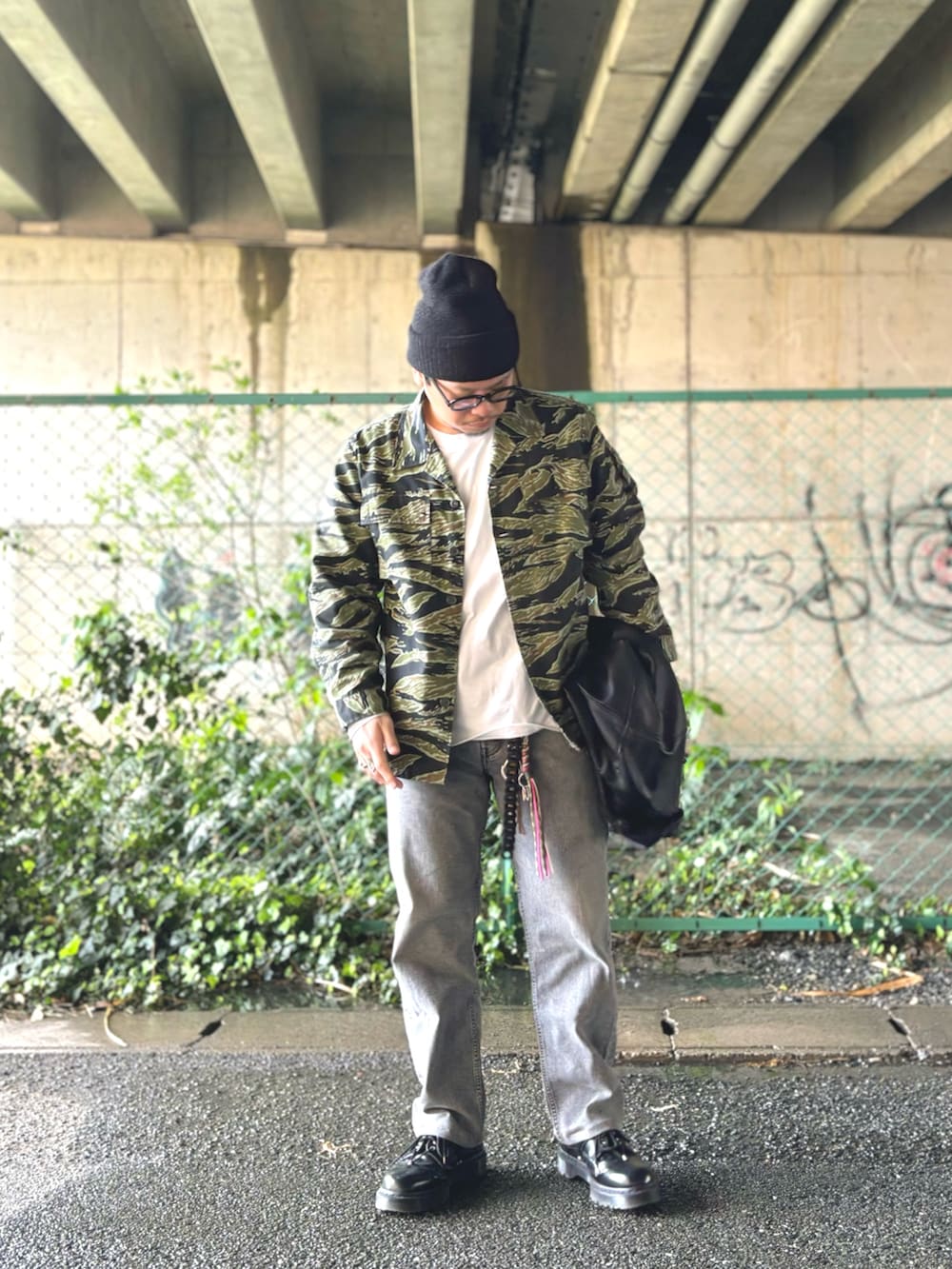 ブラック系のブルゾン、グリーン系のミリタリージャケット、グレー系のデニムパンツを着用したメンズの春コーディネートの2枚目の写真