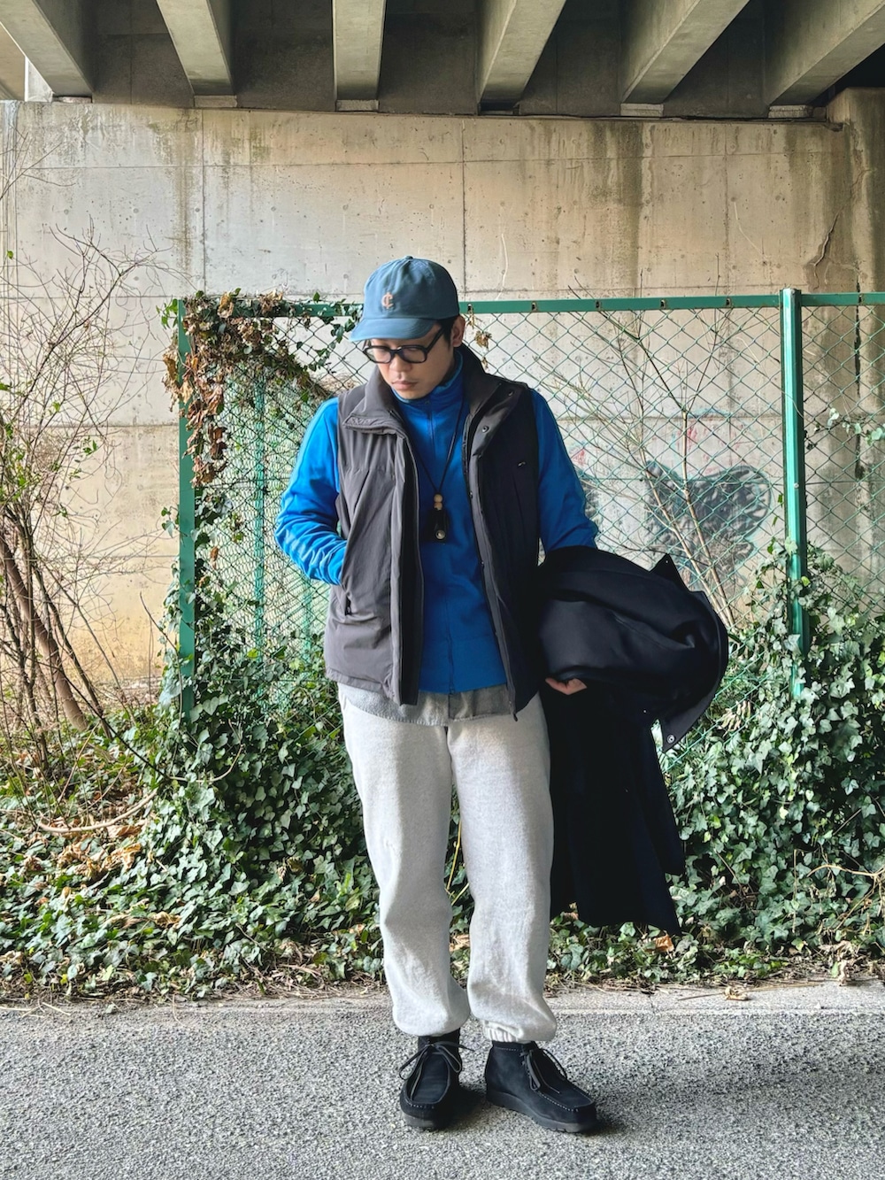 ブラック系のステンカラーコート、ブラック系のモカシン/デッキシューズ、グレー系のスウェットパンツを着用したメンズの冬コーディネートの2枚目の写真