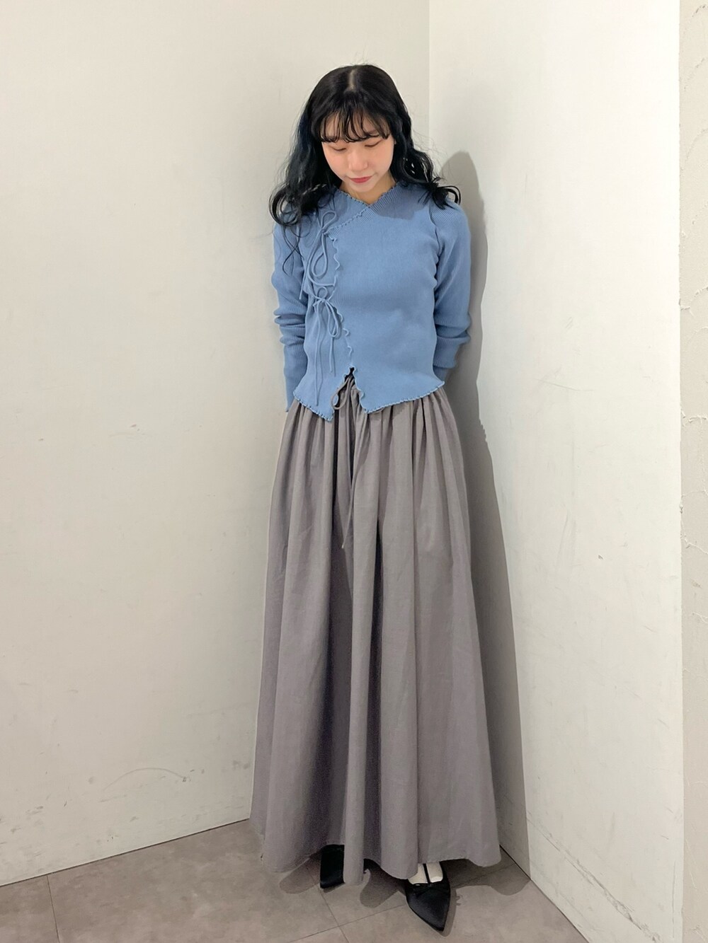 ブルー系のニット/セーター、グレー系のスカート、ブラック系のパンプスを着用したレディースの春コーディネートの2枚目の写真