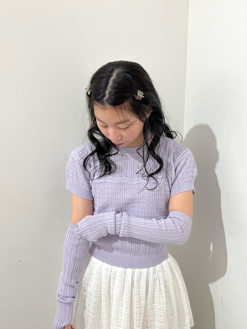 パープル系のニット/セーター、ホワイト系のスカート、シルバー系のパンプスを着用したレディースの春コーディネートの2枚目の写真