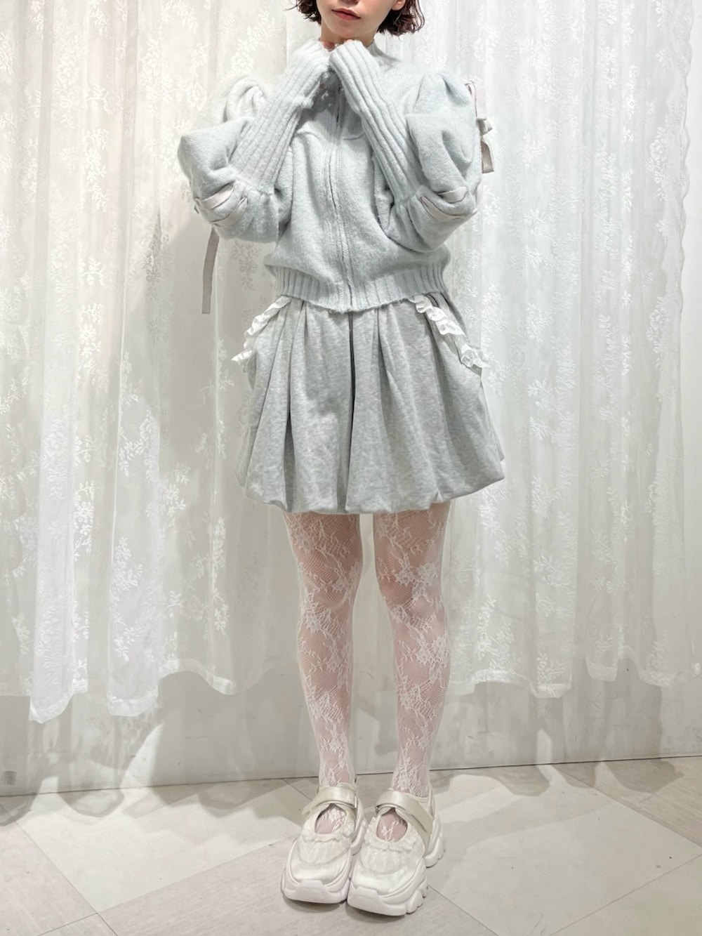 グリーン系のカーディガン/ボレロ、グレー系のスカート、ホワイト系のスニーカーを着用したレディースの秋コーディネートの2枚目の写真