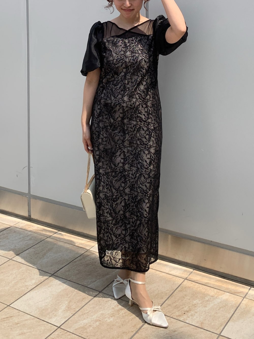 ブラック系のドレス、ブラック系のクラッチバッグ、ベージュ系のパンプスを着用したレディースの春コーディネートの2枚目の写真